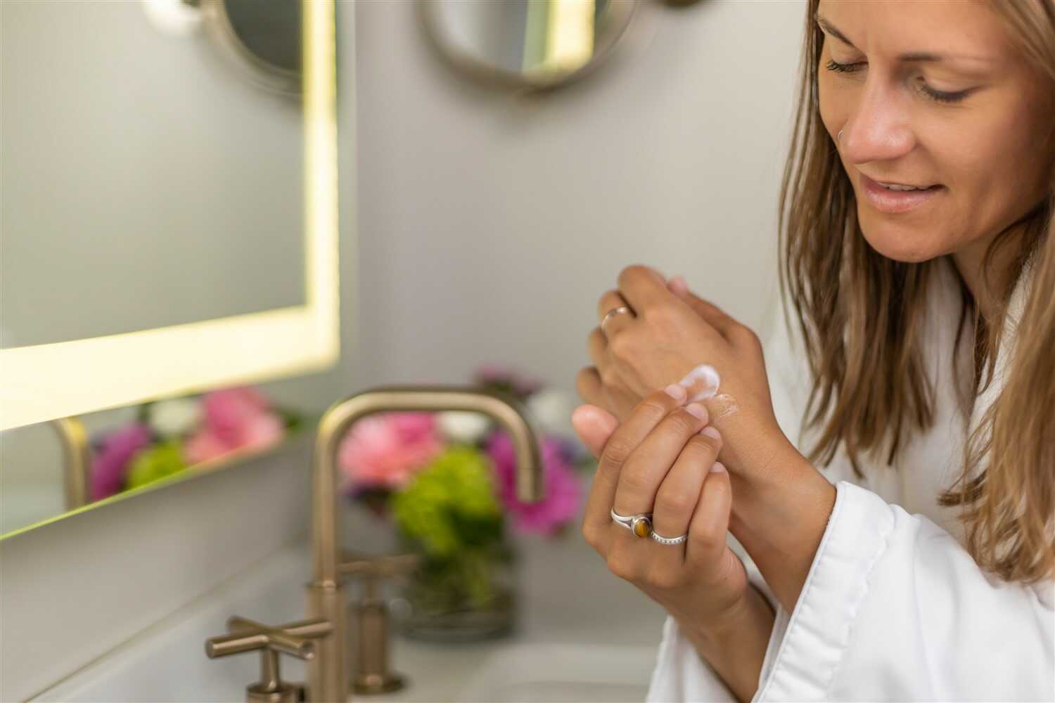 Woman applying CBD Lavender Shea Butter body cream in a bright bathroom, enhancing skin hydration and texture.