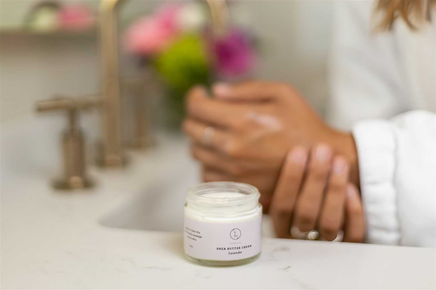 CBD Lavender Shea Butter body cream shown on a bathroom counter with hands applying lotion.