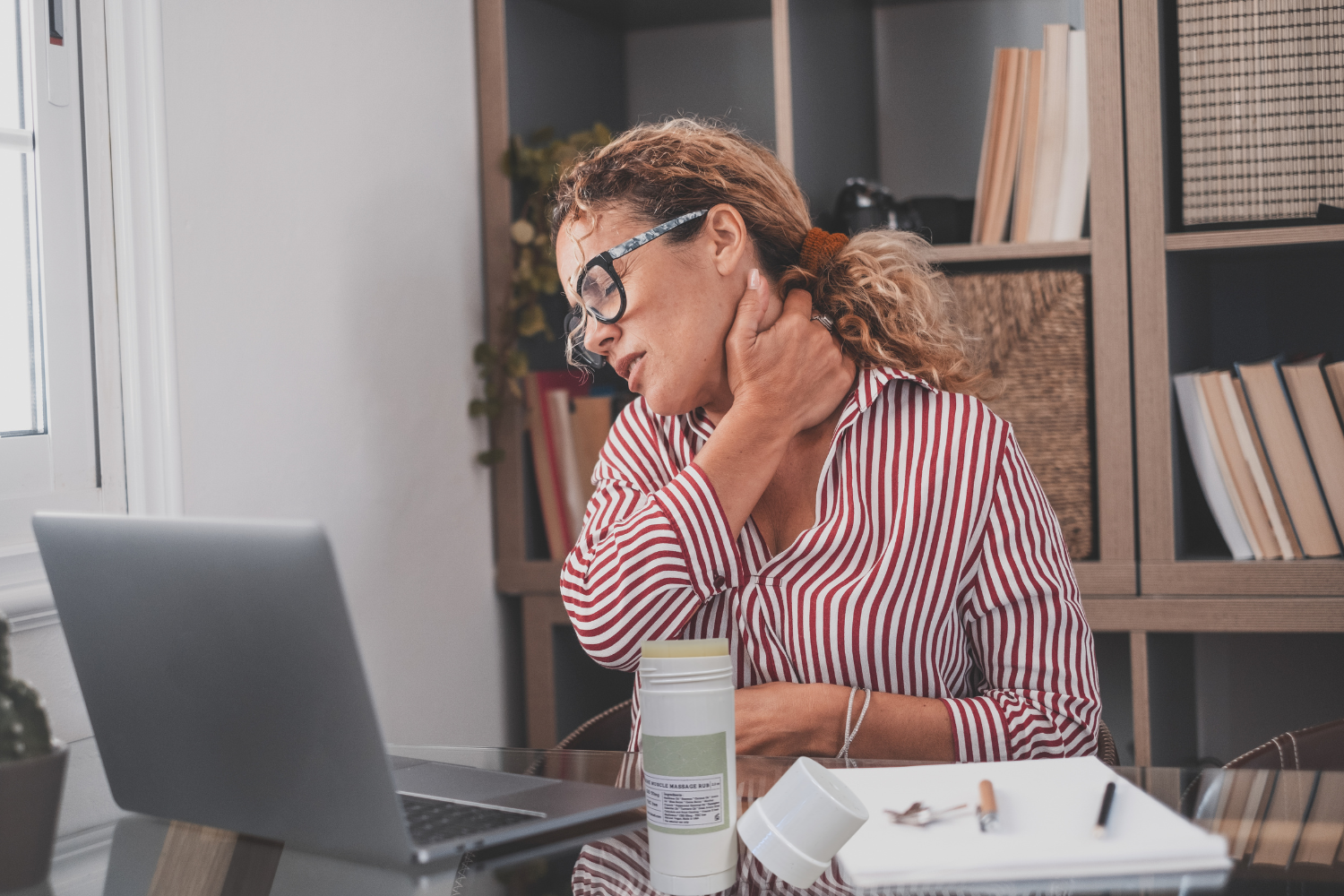 Woman with neck pain using CBD Muscle Rescue Balm while working at home on her laptop.