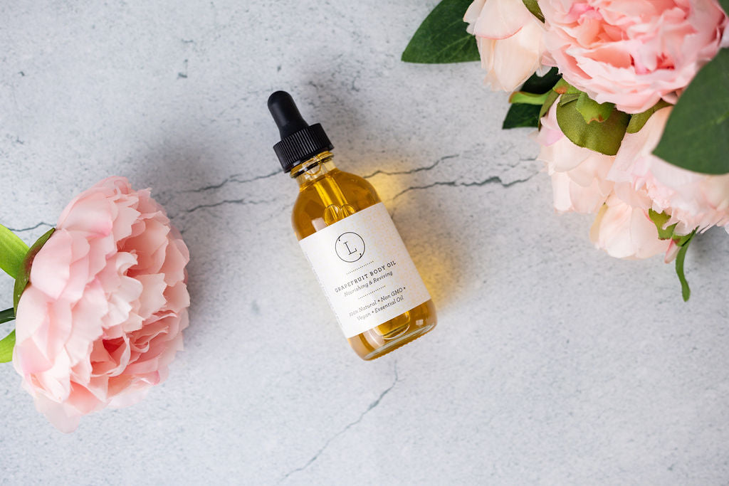 CBD Natural Body Oil bottle next to pink peonies on a marble surface, great for moisturizing and nourishing skin.