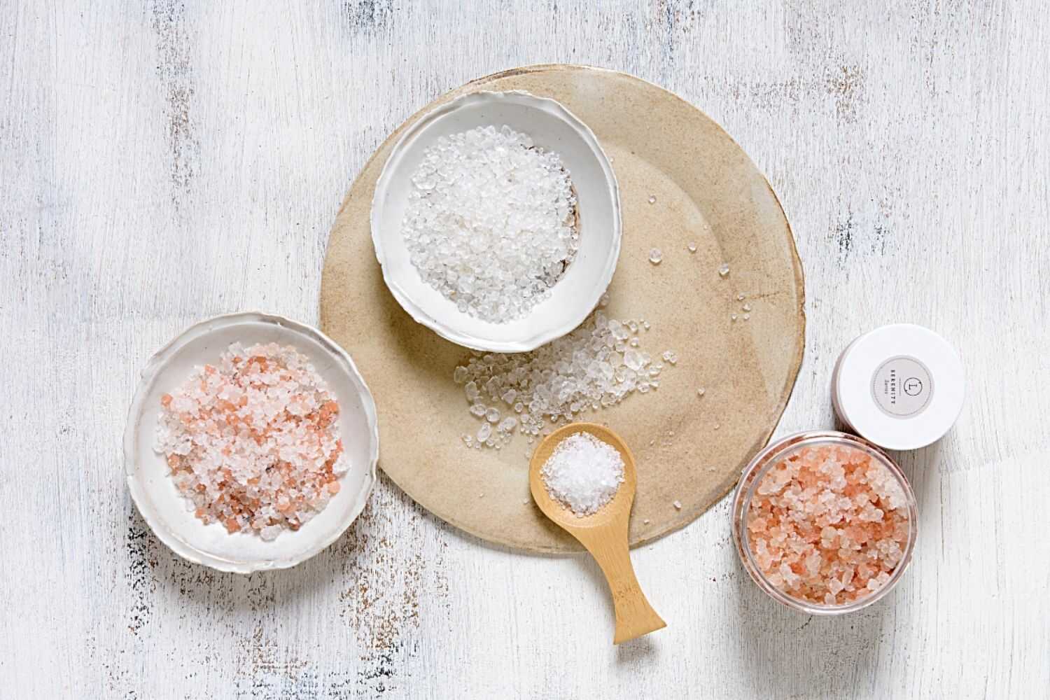 Variety of bath salts in bowls and containers, including pink Himalayan salt for soothing bath experience.